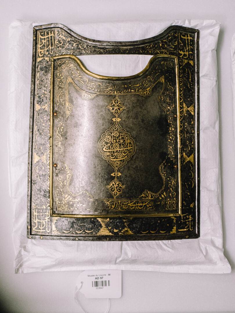 Une plaque d’armure en acier damasquiné originaire d’Iran est conservée sur un petit matelas adapté à sa forme.